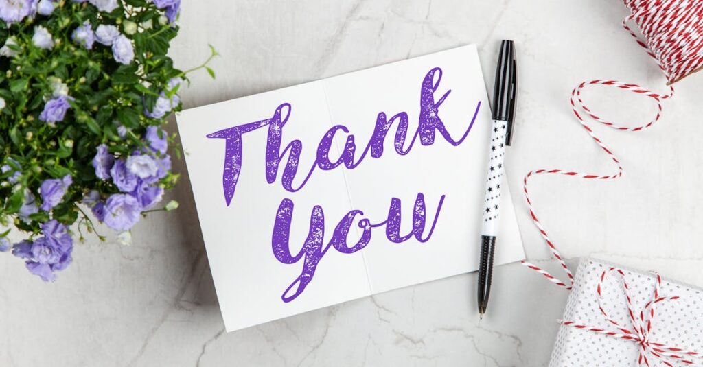 A stylish thank you card paired with purple flowers, a gift box, and pen on a marble surface.